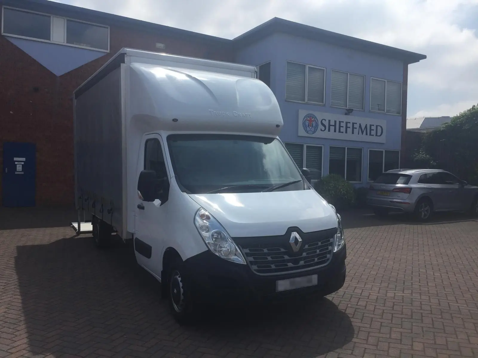 A large renault van parked outside the Sheffmed building. The Sheffmed logo and text are visible on the side of the building behind and to the right of the van.