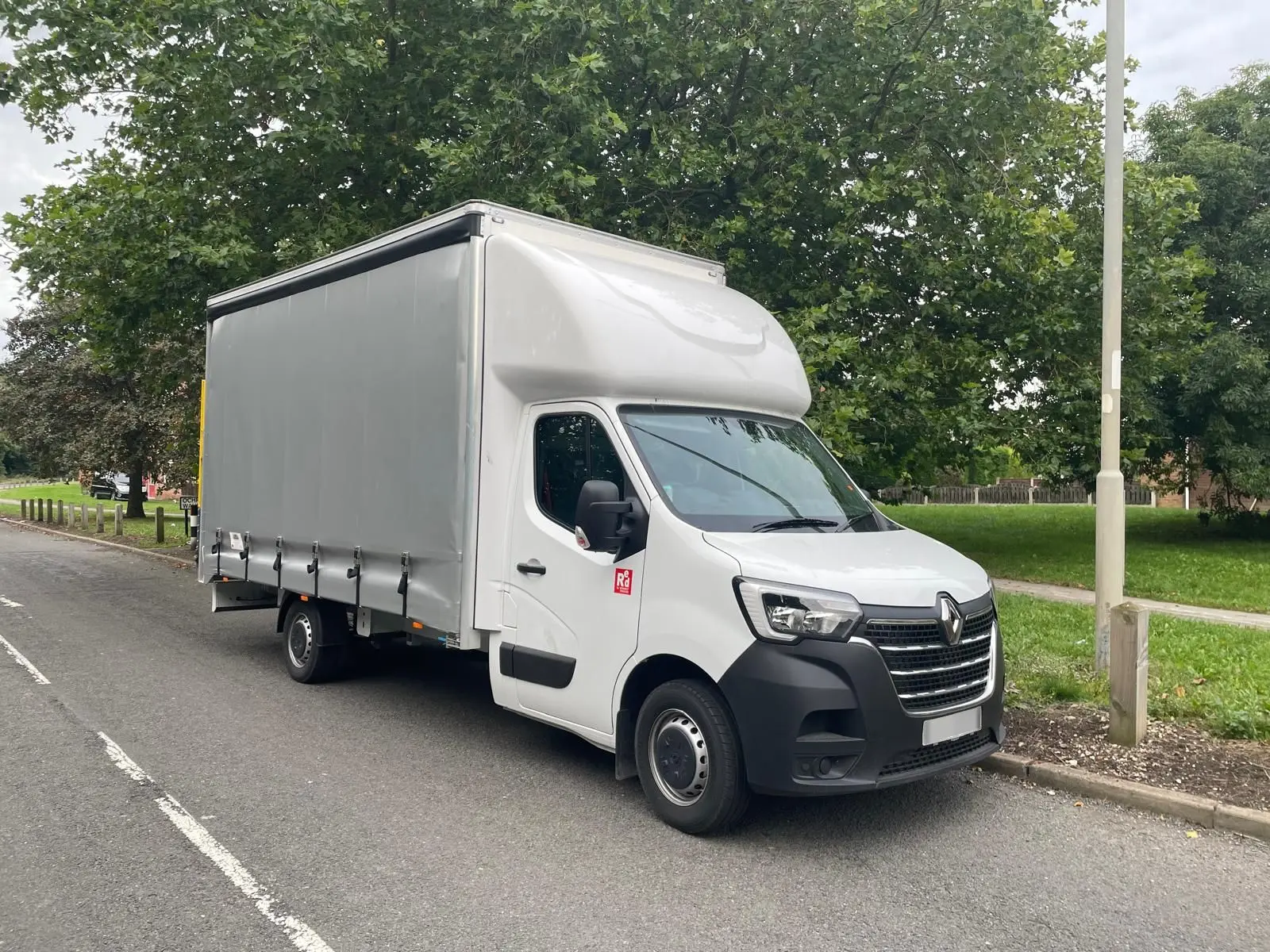 A large renault van parked curbside, the front cab is white and visible side is grey, flanked by large trees.