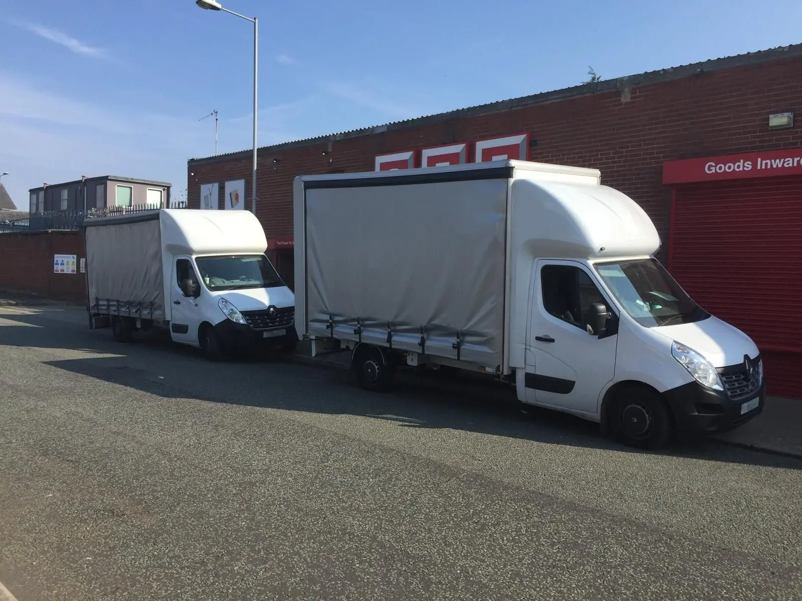 Photo with two large vans parked curbside. A shuttered door to the right of the photo is labelled 'Goods Inward'