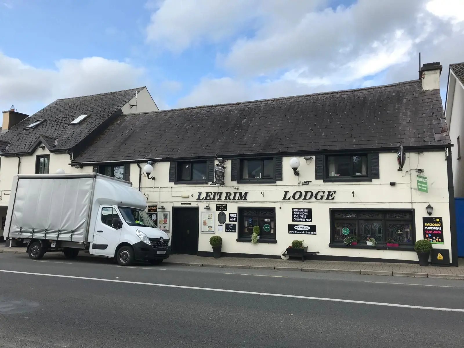 A large renault van parked curbside to deliver to Leitrim Lodge. The van takes up a third of the image width. The rest is the pub's exterior and signage.